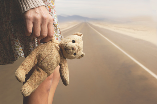 girl holds her teddy bear in hand along a road to abandon it, concept of person's growth stages in life