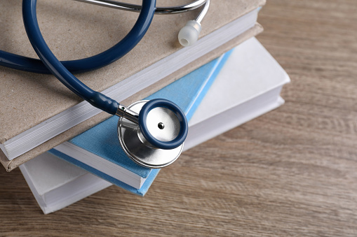 Student textbooks and stethoscope on wooden table, closeup view with space for text Medical education