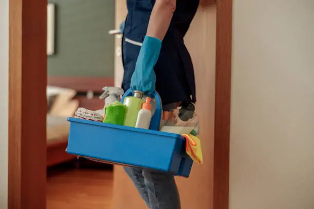 Photo of Close up of housemaid in uniform for cleaning apartment holds box with detergents and rags