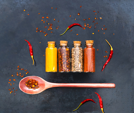 Spices in glass containers and  wooden spoon on dark background. Atmospheric mood of the Year 2023.