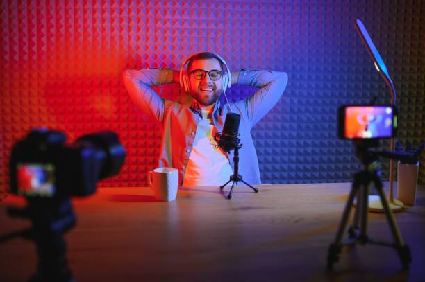 istock vlogger using smartphone to film podcast in studio. blogger with mobile phone, microphone and headphones filming video for social media broadcasting career. 1450968491