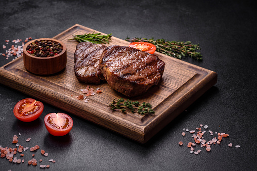 T-bone grilled beef steak with spices and herbs on wide wooden background. Top view flat lay with copy space