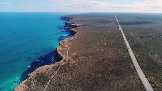 Flying above wide coastal travel scene of a car driving a straight road along the great australia bight