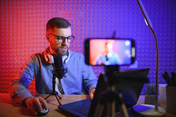 istock vlogger using smartphone to film podcast in studio. blogger with mobile phone, microphone and headphones filming video for social media broadcasting career. 1450971351