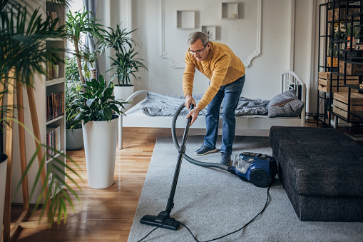 Young man with special needs vacuuming carpet at home. His girlfriend is in the background.