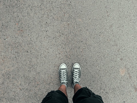 A top-view shot of a man wearing grey sneakers standing on a ground