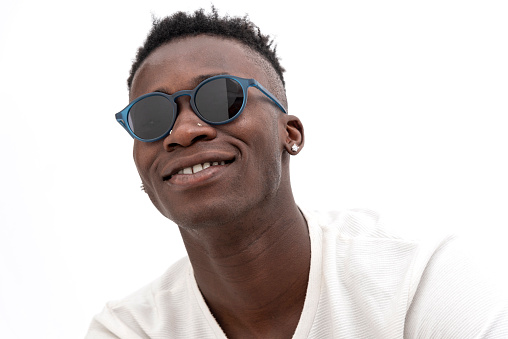 African-American man in white t-shirt wearing sunglasses against white background. Smiling looking at camera.