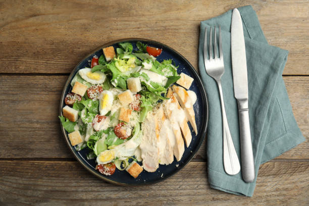 istock Delicious Caesar salad in bowl on wooden table, flat lay 1450998752