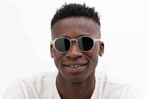 African-American man in white t-shirt wearing sunglasses against white background. Smiling looking at camera.