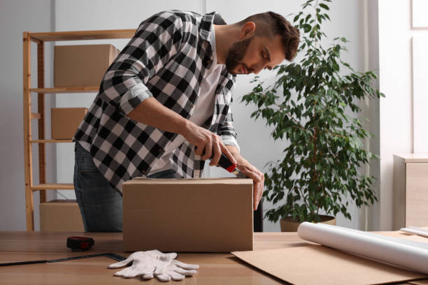 istock Man using utility knife to open parcel at wooden table indoors 1451001698
