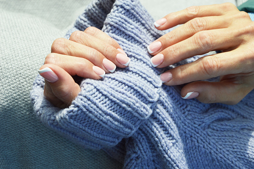 Uñas con una hermosa manicura francesa sobre el fondo de un cálido suéter de punto. Tendencia de invierno, cuidado de manos, esmalte de gel, goma laca. photo