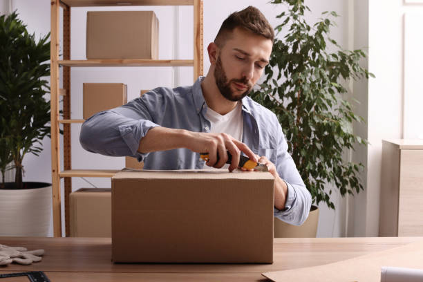 istock Man using utility knife to open parcel at wooden table indoors 1451002260