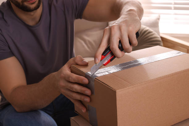 istock Man using utility knife to open parcel at home, closeup 1451002262