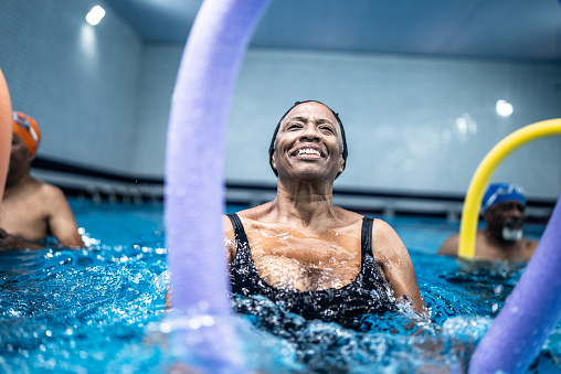 Senior woman exercising with noodle float at swimming pool