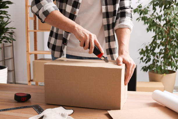 istock Man using utility knife to open parcel at wooden table indoors, closeup 1451003387