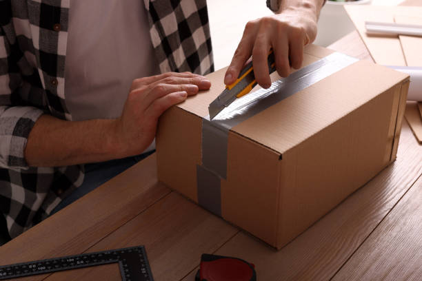 istock Man using utility knife to open parcel at wooden table, closeup 1451003783