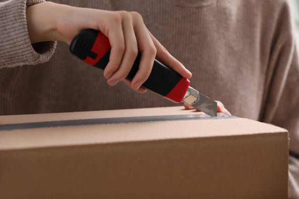 istock Young woman using utility knife to open parcel, closeup 1451004440