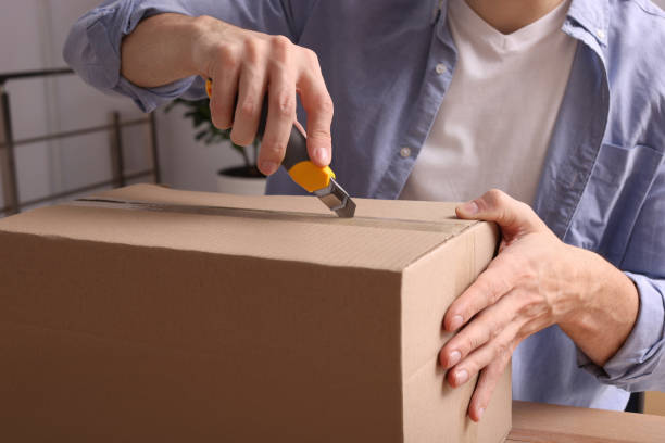 istock Man using utility knife to open parcel at wooden table indoors, closeup 1451005356