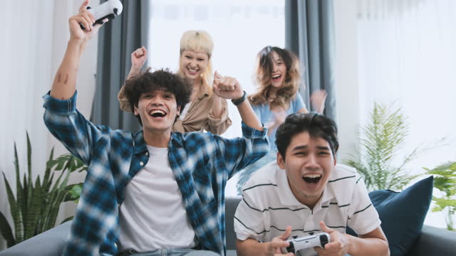 Group of happy young Asian people play console video game, laugh and smile together at home. Fun weekend leisure activity, close friends relationship, or friendship party lifestyle concept