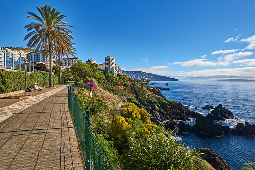 Funchal, Portugal - November 21, 2022: Pedestrians on the seafront promenade from Sao Martinho to Funchal center between hotels and flowers in winter.