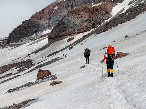 Two mountaineers ascending Kazbek 5054m mountain with backpacks and trekking poles. Caucasus, Georgia