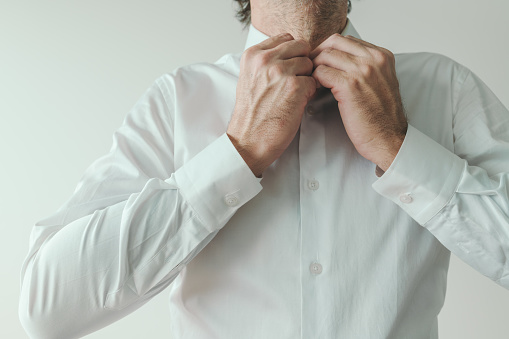 Businessman getting dressed, business person buttoning his white shirt, close up with selective focus