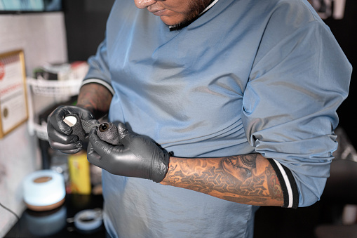 A tattoo artist is covering his tattoo machine with tape. Concept of hygiene in the tattoo studio