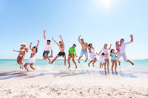 Large group of happy people having fun while jumping on the beach in summer day. Copy space.