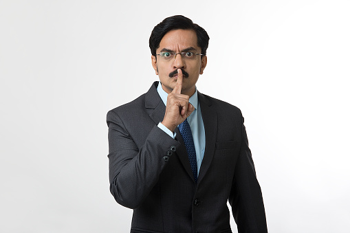 Portrait of businessman gesturing with finger on his lips showing shh quiet sign