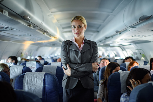 Smiling stewardess standing in an airplane with her arms crossed and looking at camera.