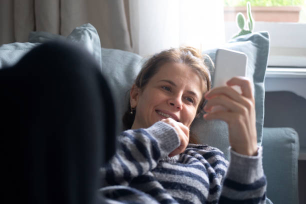 istock Beautiful woman lying on sofa and having fun while browsing social media on cell phone. 1451023894