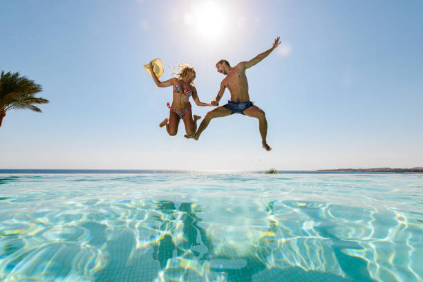 ci-dessous vue d’un couple enjoué sautant dans la piscine à débordement. - floating on water swimming pool men water photos et images de collection