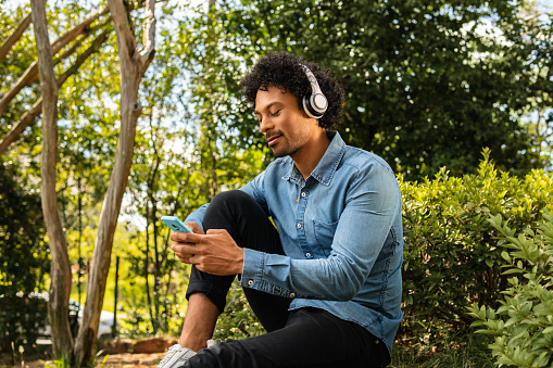black man listening music on mobile phone with headphones in the park
