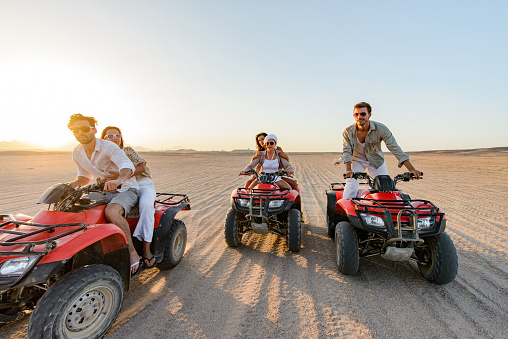 Group of happy friends having fun while driving quads in summer at the desert. Copy space.