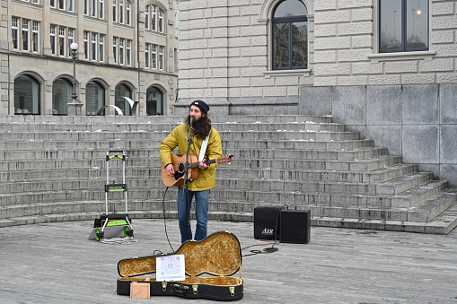 Zurich, Switzerland, 12 18 2022: Street musician singing and playing guitar in centrum of city during Christmas market. He is staying next to stairs of Theater. Guitar case is open for small money.