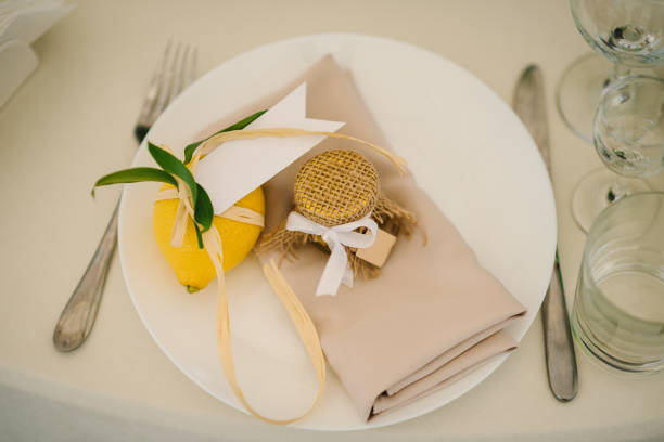 istock Banquet table served silverware, plate with napkin, cutlery and glasses. Wedding reception. Serving, setting table. Gift decorated with ribbons and branch greenery, decoration. Compliment for guests. 1451032222
