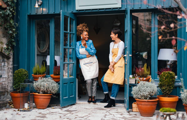 Portrait Of Two Smiling Colleagues Working Together In A Home Decor Store Happy African-American woman and her employee talking and laughing while standing at door of the store. small business stock pictures, royalty-free photos & images