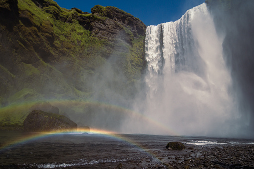 Rainbow near large waterfall landscape photo. Beautiful nature scenery photography with sky on background. Idyllic scene. High quality picture for wallpaper, travel blog, magazine, article