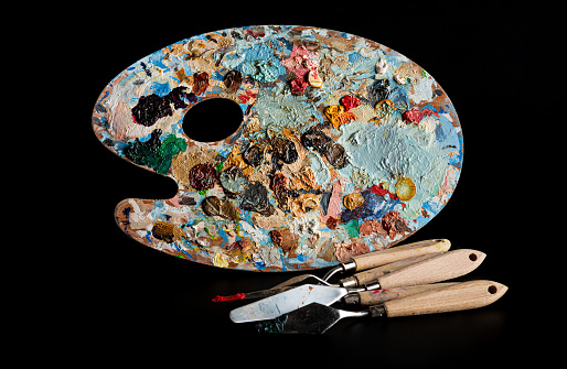Wooden palette with beautiful spots of oil paint and palette knives highlighted on a black background