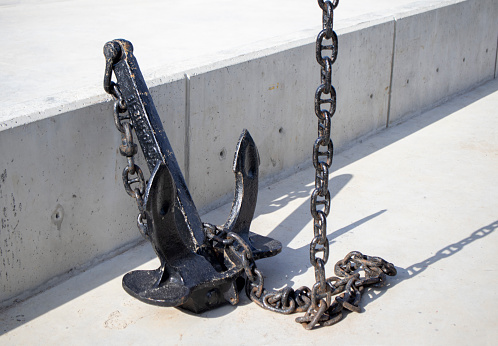 Rusty anchor chain. Stud link type ship chain connected to mooring bollard on ferry port by seaside. Large, heavy, old iron rope lays encrusted in rust. Vintage style nautical equipment in charge of vessel safety.