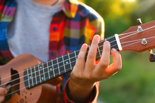 Defocus woman is learning to play the ukulele. Girl tunes a miniature guitar before a concert. Outside. Out of focus.