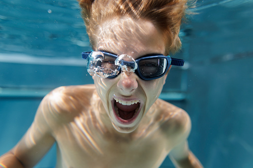 Portrait of a crazy teenage boy shouting underwater in the swimming pool\nShot with Canon R5.