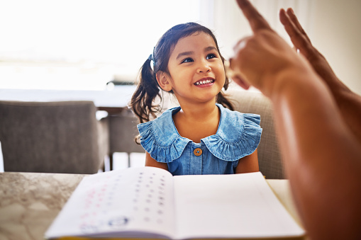 Education, homeschool and a kindergarten girl with smile, notebook and help from mother in math class. Home school, happy child and learning to count on fingers and hands, woman teaching kid maths.