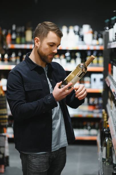 Portrait of young glad positive male customer selecting wine in supermarket Portrait of young glad positive male customer selecting wine in supermarket. wine shipping stock pictures, royalty-free photos & images