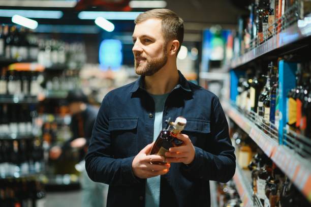 男はスーパーマーケットの棚からアルコール飲料を取ります。店内でお酒を買う。 - whisky alcohol bottle hard liquor ストックフォトと画像