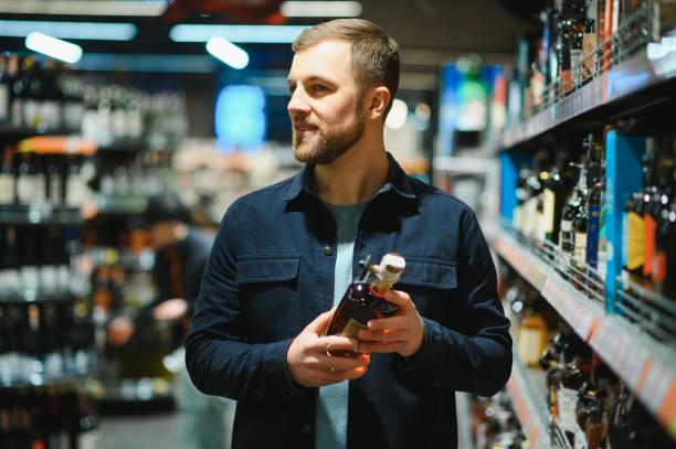 A man takes alcoholic drinks from the supermarket shelf. Shopping for alcohol in the store. A man takes alcoholic drinks from the supermarket shelf. Shopping for alcohol in the store alcohol shop stock pictures, royalty-free photos & images