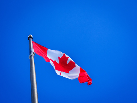Canadian flag waving in the wind against the blue sky