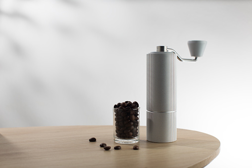 Manual coffee grinder and dark roast coffee beans on wood table