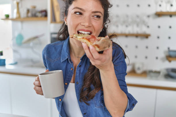 istock Smiling young woman using her mobile phone while drinking a cup of coffee in the kitchen at home 1451068003