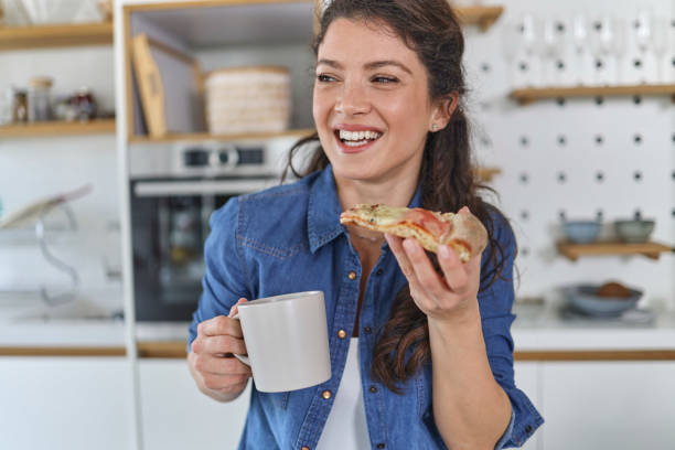 istock Smiling young woman using her mobile phone while drinking a cup of coffee in the kitchen at home 1451068027